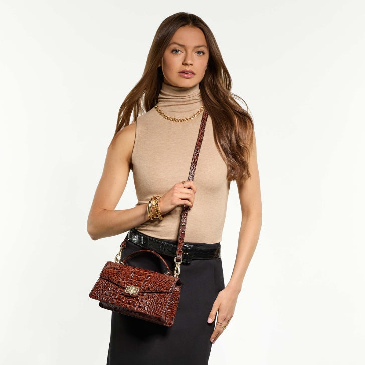 Model wearing a beige sleeveless turtleneck carrying a structured brown crocodile embossed handbag with a top handle and long shoulder strap.